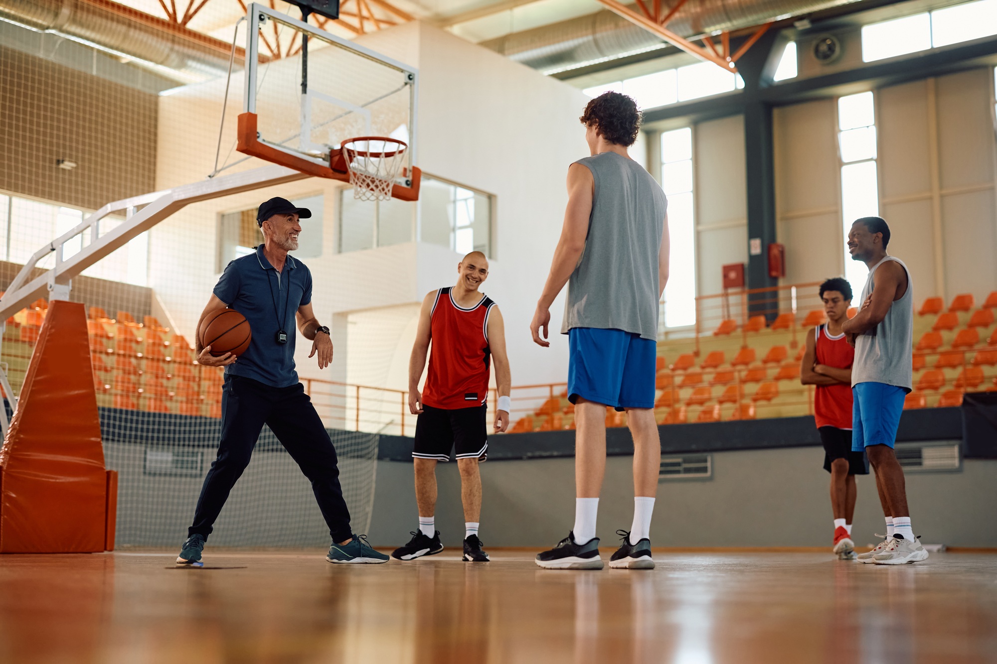 Happy basketball coach with players during sports training at school gymnasium.