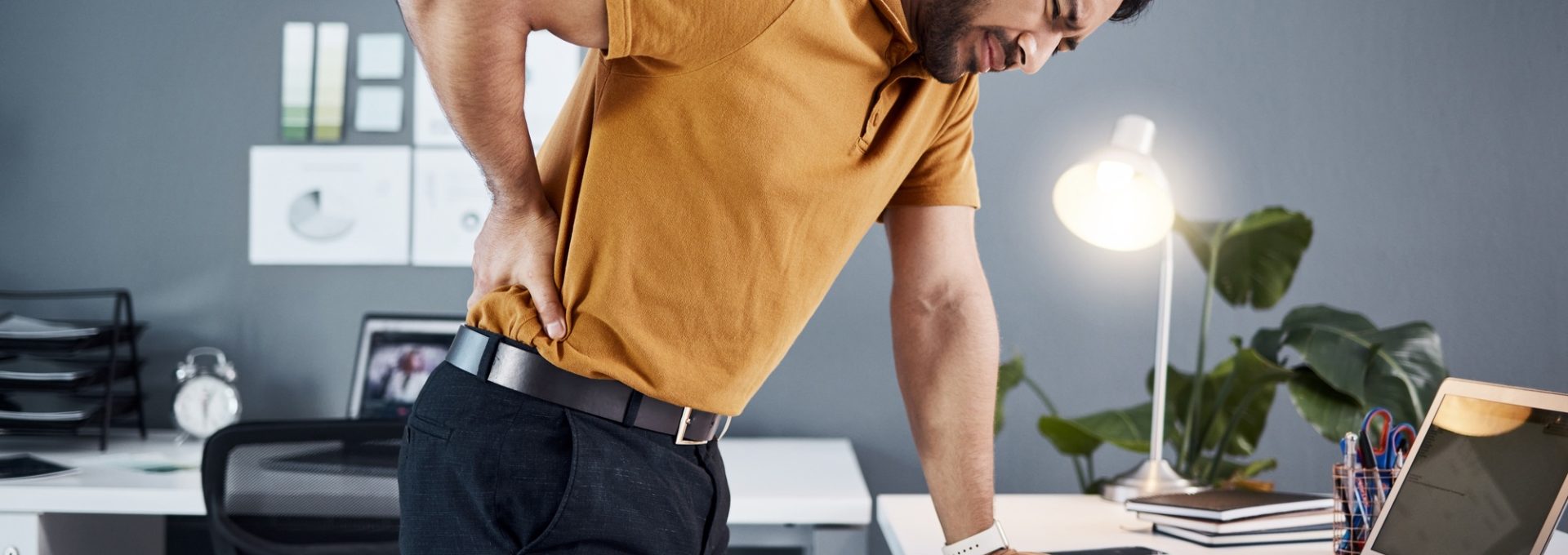 Night, back pain and business man with stress at office desk with a laptop and depression. Professi